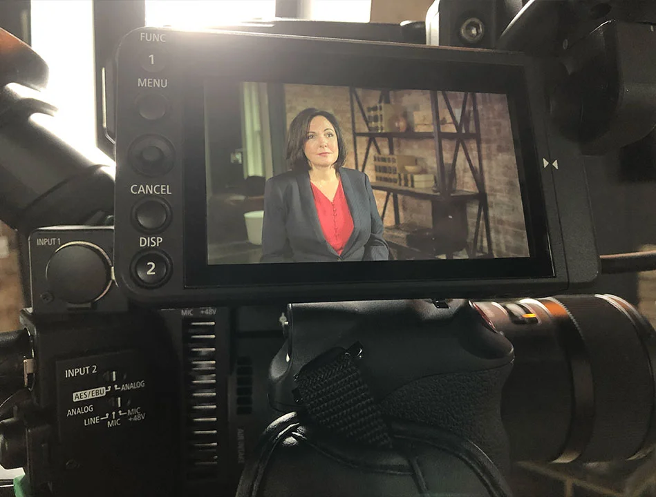 Attorney Cyndi Crocker is looking at an interview subject on a camera LED screen discussing legal matters wearing a red shirt and navy blazer