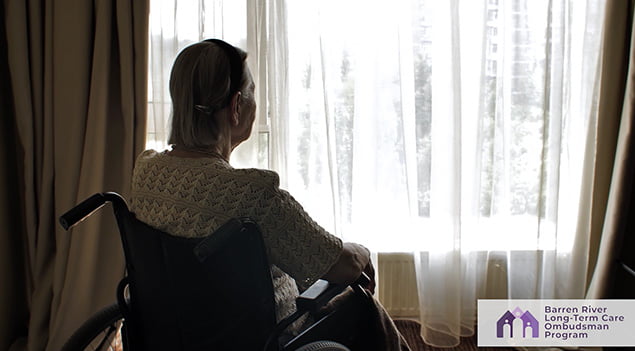 elderly woman looks out the window at a nursing home facility